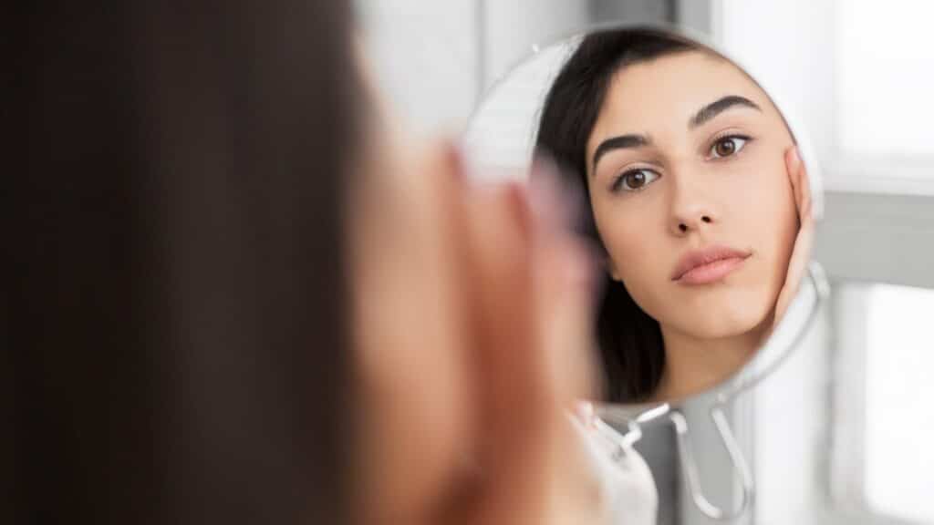 Chica tocando la cara mirando a la piel perfecta en el espejo, Panorama
